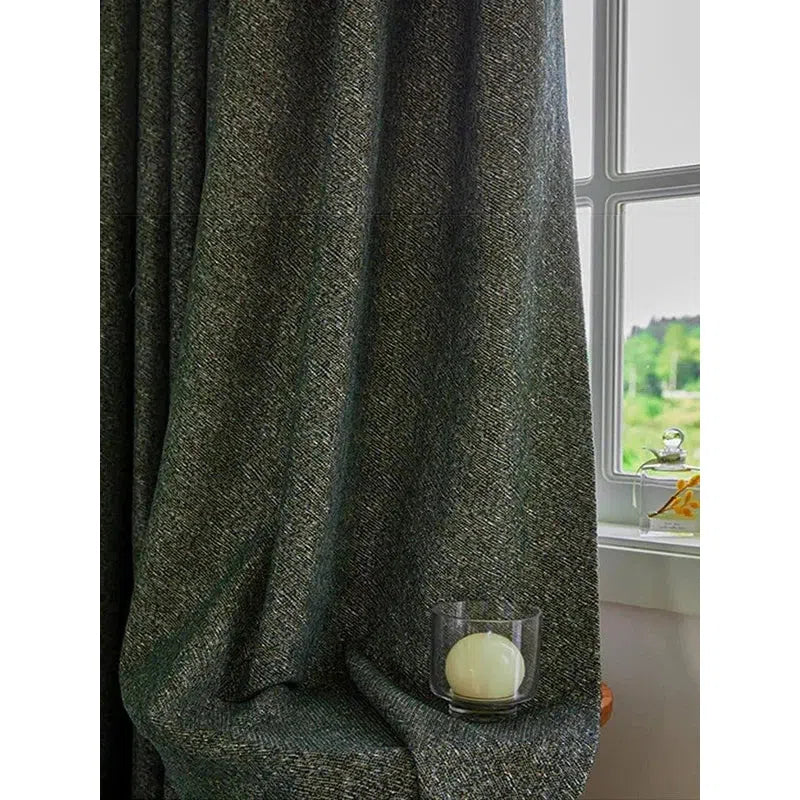 Rideau épais gris foncé drapé dans un intérieur lumineux, accentuant l'élégance d'une pièce. Accessoire déco avec bougie dans son support en verre, créant une ambiance chaleureuse près de la fenêtre ouverte avec vue sur un paysage verdoyant. Idéal pour ajouter une touche sophistiquée à votre salon ou chambre.