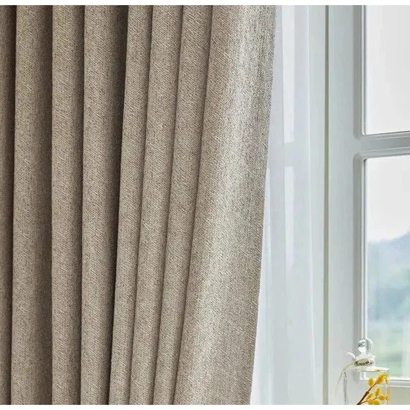Rideau élégant beige devant une fenêtre, idéal pour le salon ou la chambre. Offre une isolation lumineuse optimale et ajoute une touche de sophistication à votre intérieur. Solution pratique pour améliorer l'ambiance de votre maison.