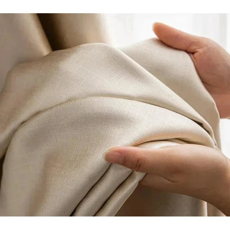 Image d'un rideau beige élégant tenu par des mains, offrant une vue détaillée de sa texture douce et luxueuse. Ce rideau est idéal pour ajouter une touche raffinée et chaleureuse à votre intérieur, tout en assurant une occultation modérée de la lumière. Parfait pour les salons, chambres ou bureaux, il s'intègre harmonieusement dans tout type de décoration.
