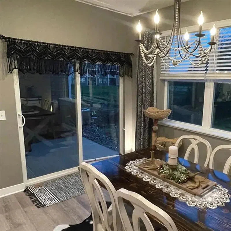 Salle à manger élégante avec une table en bois foncé décorée d'un chemin de table en dentelle, chaises au design classique, un lustre sophistiqué avec des bougies électrifiées, et une grande baie vitrée offrant une vue sur l'extérieur. Ambiance chaleureuse et décor raffinée pour des repas conviviaux.