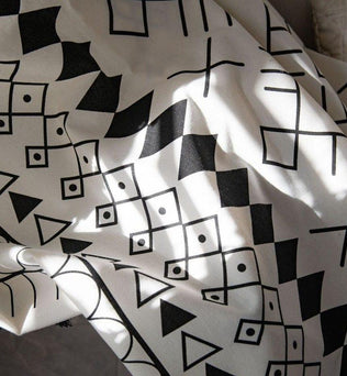 Tissu décoratif avec motifs géométriques noirs sur fond blanc, idéal pour ajouter une touche moderne à votre intérieur. Ce design unique combine des formes abstraites, parfait pour un salon contemporain ou une chambre tendance. Personnalisez votre espace avec cet élément décoratif chic.