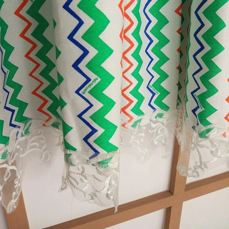 Rideau décoratif à motifs géométriques colorés, verts, bleus et oranges, avec une élégante bordure en dentelle blanche parfaite pour habiller vos fenêtres et apporter une touche moderne et raffinée à votre intérieur. Idéal pour un salon ou une chambre, ce rideau design combine style et originalité.