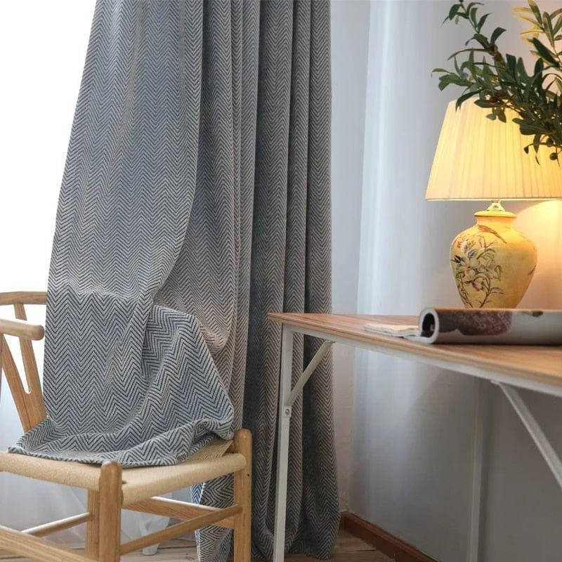 Rideau à motifs chevrons gris et blancs, suspendu dans un intérieur élégant. Il encadre harmonieusement une fenêtre, ajoutant sophistication et style. Parfait pour créer une ambiance chaleureuse et accueillante, tout en offrant une intimité optimale pour tout type d'intérieur moderne.
