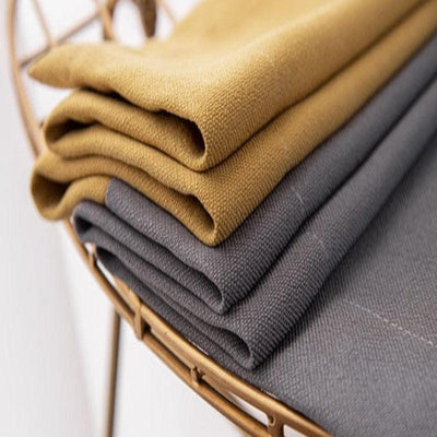 Empilement de tissus pliés de couleur moutarde et gris sur une étagère dorée, idéal pour décoration intérieure ou confection de vêtements. Ces textiles ajoutent une touche élégante et moderne à tout espace.