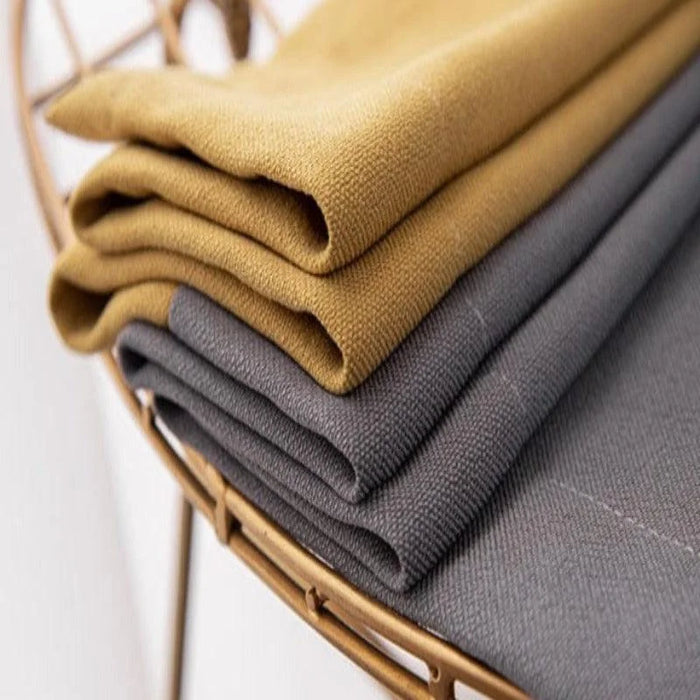 Empilement de tissus pliés de couleur moutarde et gris sur une étagère dorée, idéal pour décoration intérieure ou confection de vêtements. Ces textiles ajoutent une touche élégante et moderne à tout espace.