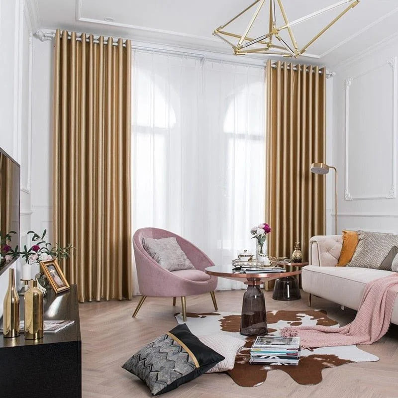 Salon moderne et élégant avec des rideaux dorés, fauteuil rose, canapé beige et accessoires décoratifs raffinés. Ambiance cosy et chic, idéale pour un intérieur tendance et accueillant.