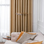 Salon élégant avec un canapé beige et des coussins décoratifs colorés assortis à un rideau doré. Une lampe moderne se tient à côté, offrant une ambiance chaleureuse et accueillante. Parfaite combinaison de design intérieur et confort, idéale pour un espace de vie sophistiqué.