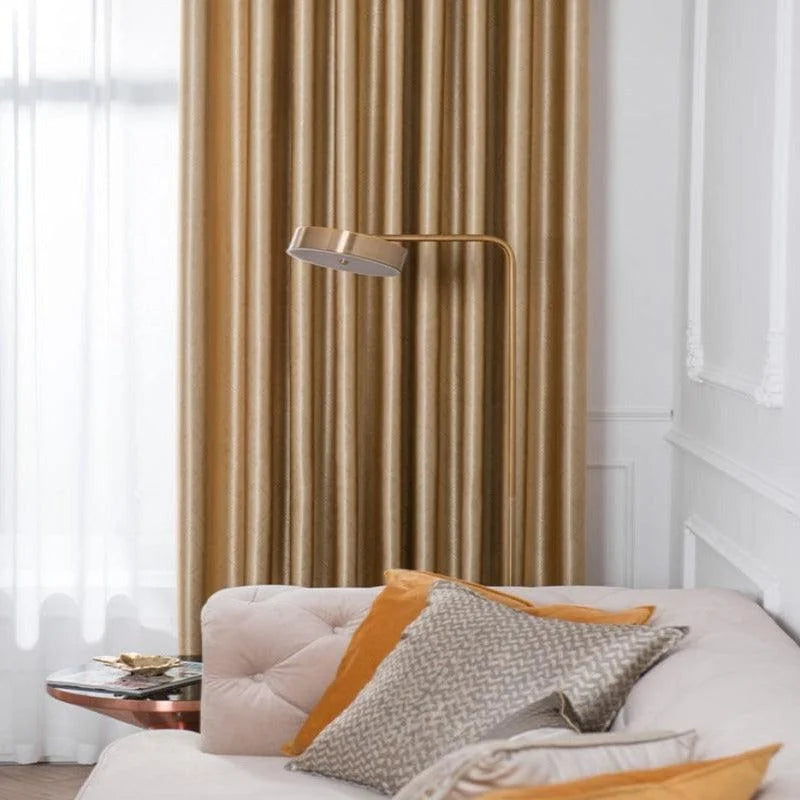 Salon élégant avec un canapé beige et des coussins décoratifs colorés assortis à un rideau doré. Une lampe moderne se tient à côté, offrant une ambiance chaleureuse et accueillante. Parfaite combinaison de design intérieur et confort, idéale pour un espace de vie sophistiqué.
