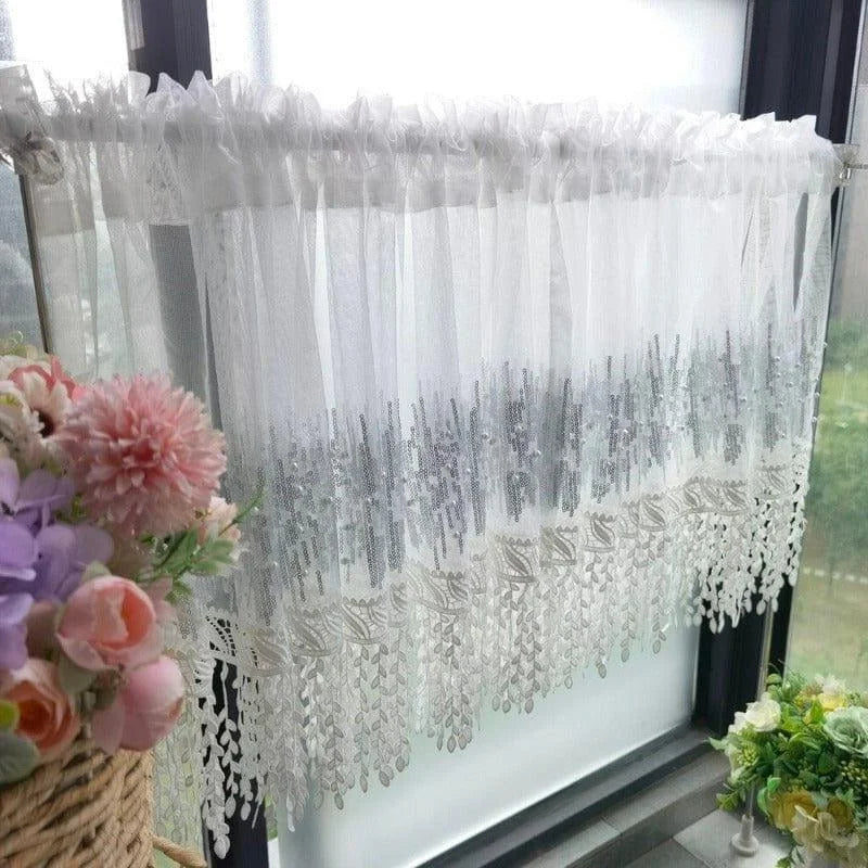 Rideau de fenêtre élégant blanc avec ornements argentés, idéal pour ajouter une touche de sophistication à votre intérieur. Parfait pour les petites fenêtres, il permet de filtrer la lumière tout en préservant l'intimité. Accessoire décoratif, ce rideau s'harmonise aisément avec différents styles de décoration intérieure. Plantes en fleurs à proximité pour un effet naturel et apaisant.