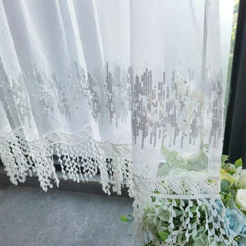 Rideau blanc élégant avec motifs brodés et détails en dentelle, idéal pour embellir un salon lumineux. Accessoire de décoration qui apporte une touche chic et sophistiquée à votre intérieur, tout en filtrant la lumière naturelle.