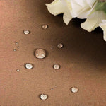 Image d'un textile déperlant marron avec des gouttes d'eau démontrant son imperméabilité, accompagné de fleurs blanches élégantes, idéal pour la décoration intérieure et la protection des meubles contre les liquides.