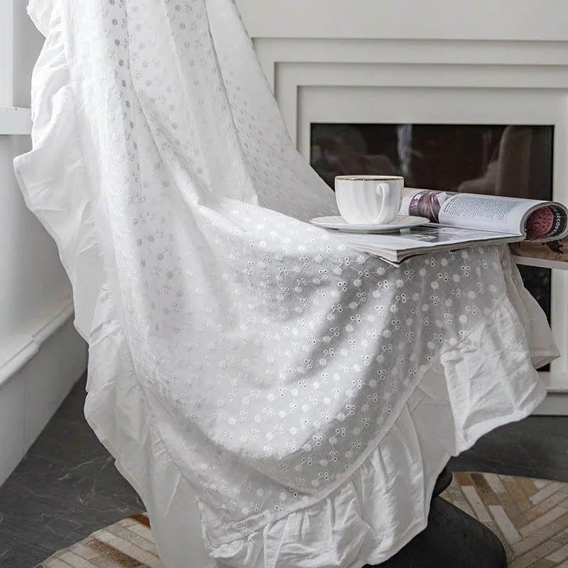 Textile d'intérieur blanc élégant avec motifs brodés, offert sur un fauteuil près d'une fenêtre, pour une ambiance de détente. Parfait pour créer un coin lecture confortable avec une touche décorative raffinée, accompagné d'une tasse de café et d'un magazine ouvert. Idéal pour ajouter une touche de luminosité et d'élégance à votre salon ou chambre.