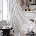 Voilage blanc élégant pour salon moderne, drapé près de la fenêtre pour filtrer la lumière naturelle, avec finitions à volants. Idéal pour un décor intérieur raffiné, ce rideau offre une touche de sophistication à votre espace de vie. Accessoire essentiel pour une ambiance lumineuse et confortable.