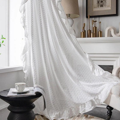 Voilage blanc élégant pour salon moderne, drapé près de la fenêtre pour filtrer la lumière naturelle, avec finitions à volants. Idéal pour un décor intérieur raffiné, ce rideau offre une touche de sophistication à votre espace de vie. Accessoire essentiel pour une ambiance lumineuse et confortable.