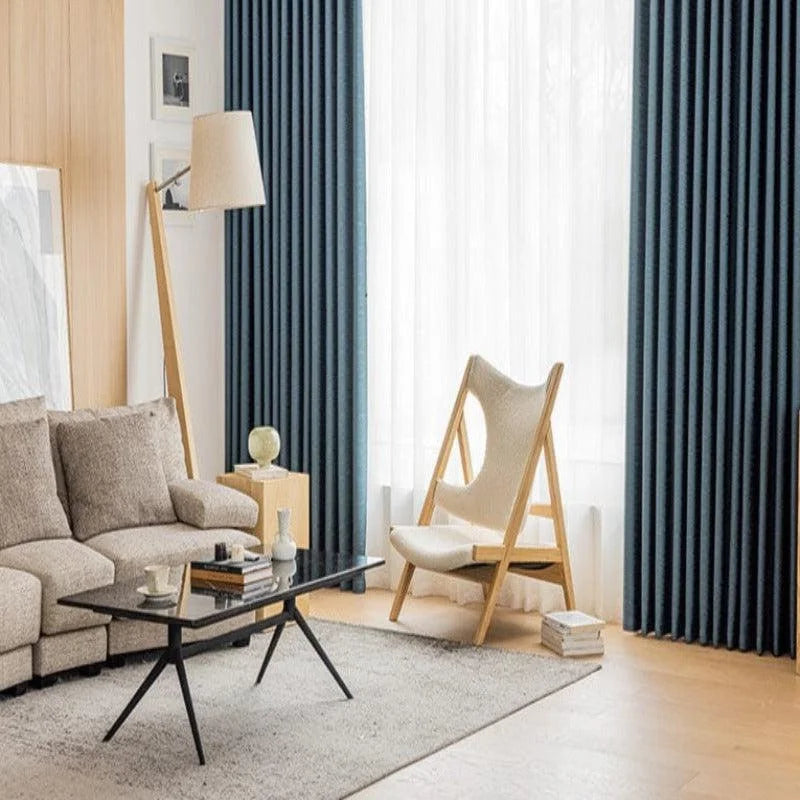 Salon moderne et élégant avec des rideaux sombres accentuant la luminosité de la pièce. Un canapé confortable s’accompagne d'une chaise design et d'une table basse au style contemporain. Parfait pour créer un espace de détente chic et accueillant, idéal pour sublimer votre intérieur.