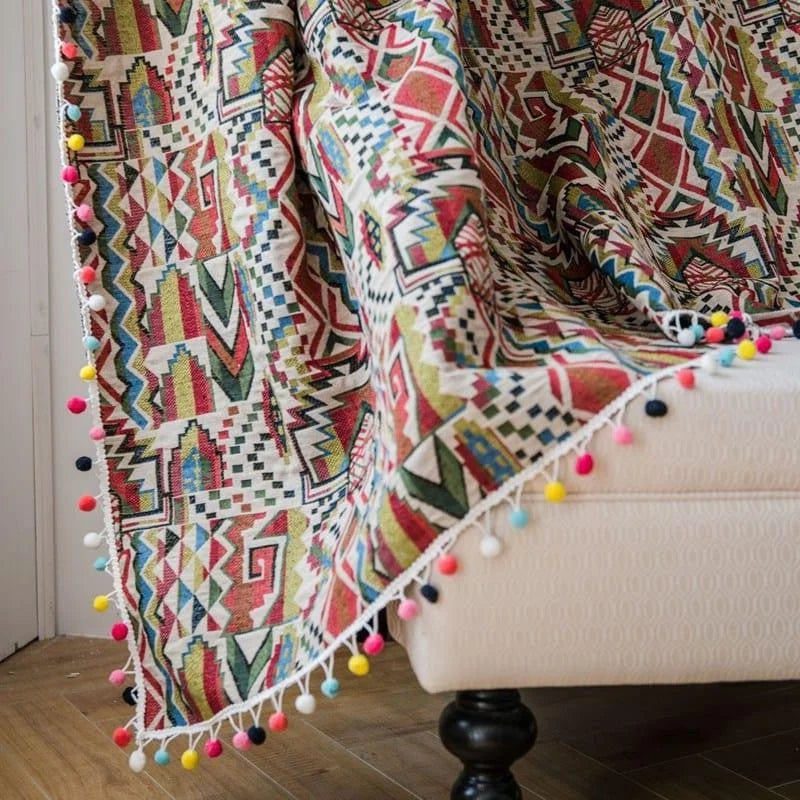 Jeté de canapé avec motifs géométriques colorés et pompons, relooking pour salon moderne et tendance, accessoire déco multicouleur pour une touche bohème.