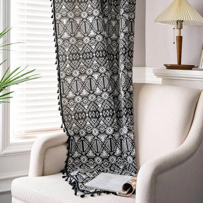 Plaid noir et blanc avec motifs géométriques, décoré de franges, posé sur un fauteuil beige dans un salon lumineux. Idéal pour ajouter une touche contemporaine à votre intérieur tout en apportant confort et chaleur. Parfait pour les soirées cocooning ou comme élément de décoration esthétique.