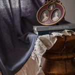 Image d'un intérieur élégant et raffiné présentant une table basse en bois ornée de livres d'art, un cadre photo ovale vintage avec trois portraits et un textile drapé. L'atmosphère crée une ambiance chaleureuse et artistique, idéale pour une décoration intérieure sophistiquée et chic.