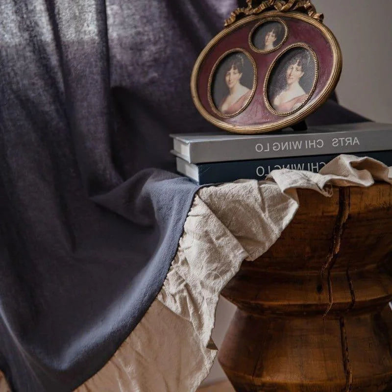 Image d'un intérieur élégant et raffiné présentant une table basse en bois ornée de livres d'art, un cadre photo ovale vintage avec trois portraits et un textile drapé. L'atmosphère crée une ambiance chaleureuse et artistique, idéale pour une décoration intérieure sophistiquée et chic.