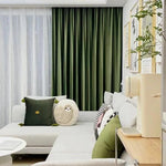 Salon moderne avec rideaux verts, canapé gris clair avec coussins décoratifs. Décoration murale tendance avec cadres, ambiance accueillante et confortable idéale pour se détendre.