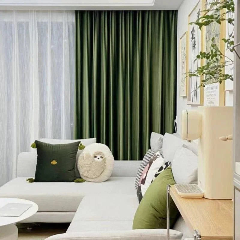 Salon moderne avec rideaux verts, canapé gris clair avec coussins décoratifs. Décoration murale tendance avec cadres, ambiance accueillante et confortable idéale pour se détendre.