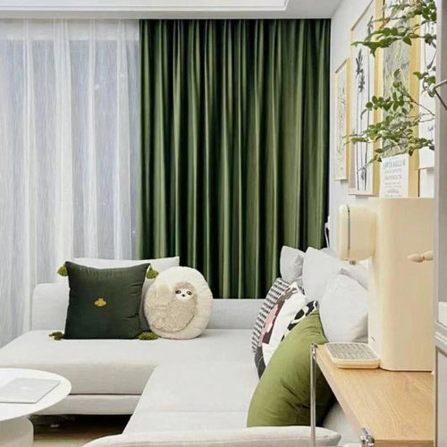 Salon moderne avec rideaux verts, canapé gris clair avec coussins décoratifs. Décoration murale tendance avec cadres, ambiance accueillante et confortable idéale pour se détendre.