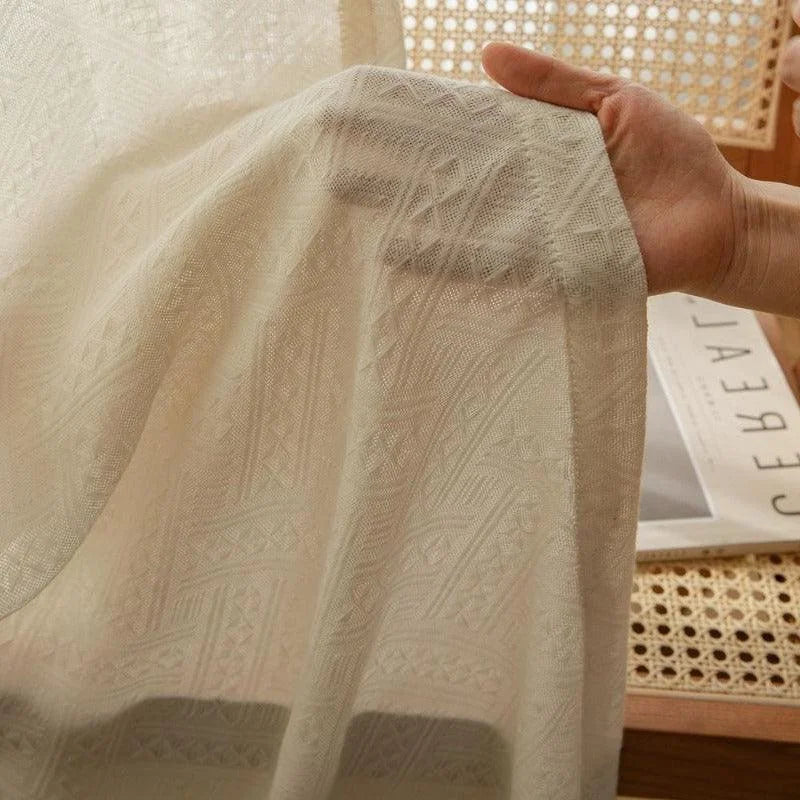Génère une image mettant en avant un tissu délicat avec des motifs géométriques sophistiqués. La main en arrière-plan souligne la finesse et la qualité de l'article. Produit idéal pour ajouter une touche élégante à votre intérieur, combinant style et fonctionnalité.