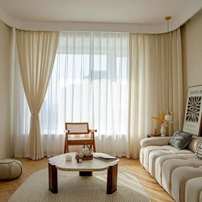 Salon moderne et lumineux avec un canapé élégant, une table basse au design contemporain, et une décoration épurée. Ambiance minimaliste et chaleureuse, parfaite pour un espace de détente et de convivialité. Rideaux de couleur claire laissant entrer une douce lumière naturelle, accentuant l'atmosphère apaisante de la pièce. Idéal pour les amateurs de décoration intérieure chic et moderne.