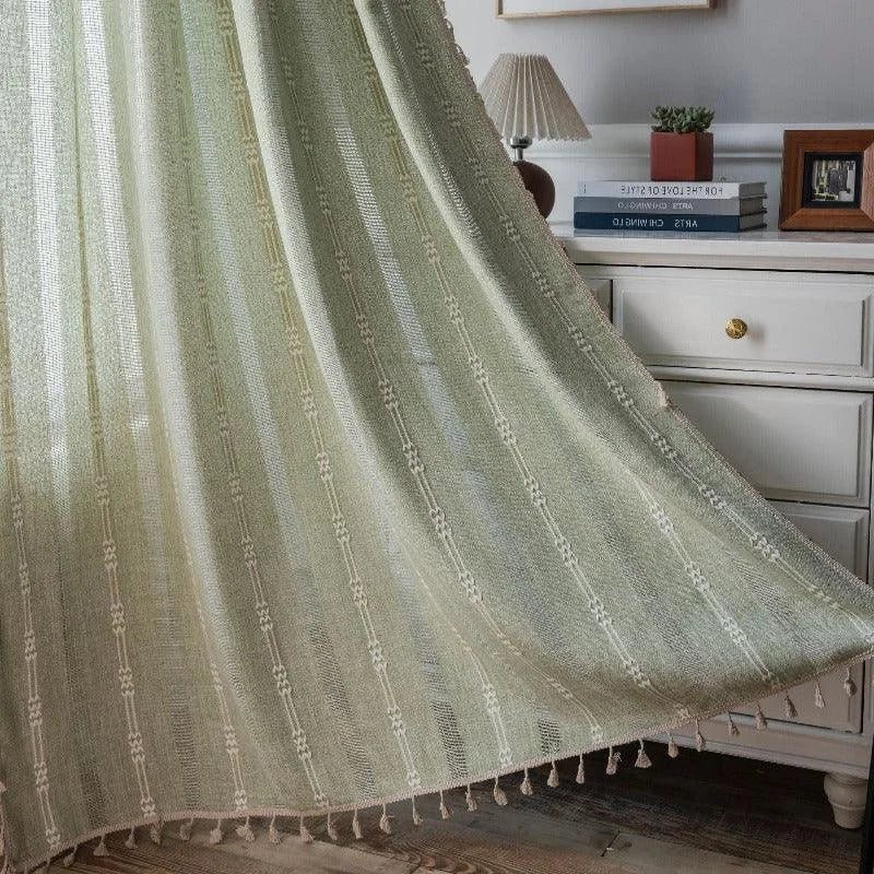 Rideau décoratif vert pastel avec motifs géométriques, idéal pour apporter une touche d'élégance et de simplicité à votre intérieur. Ce rideau s'adapte parfaitement à une décoration de chambre ou de salon, offrant une lumière douce et tamisée. Il est accentué par de délicates franges pour un style raffiné.