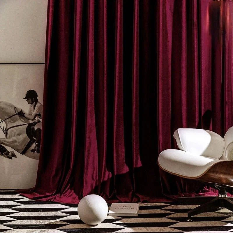 Rideau élégant de couleur bordeaux apportant une touche sophistiquée à un intérieur moderne, accompagné d'un fauteuil design blanc et d'éléments décoratifs artistiques, créant une ambiance chic et contemporaine.