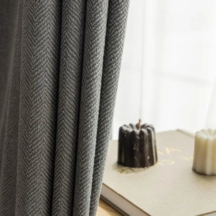 Rideaux élégants gris à motif chevron devant une fenêtre lumineuse avec décoration de livres et bougies, idéals pour une décoration intérieure moderne et sophistiquée.