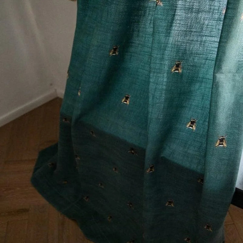 Robe élégante vert foncé avec motifs dorés, drapée artistiquement sur un sol en parquet. Idéale pour soirées chic, elle offre un look raffiné et sophistiqué qui attire l'attention.
