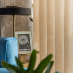 Fauteuil confortable bleu dans un salon moderne avec un lampadaire élégant, un guéridon en métal doré, et des rideaux beige. Un cadre photo avec une fleur de pissenlit est posé sur la table, ajoutant une touche artistique à la décoration intérieure. Ambiance chaleureuse et accueillante idéale pour un espace détente.