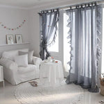 Rideaux élégants dans un salon moderne avec une ambiance lumineuse et apaisante. Le décor comprend un fauteuil confortable, une petite table ronde blanche et un tapis assorti, parfait pour créer un espace détente. Le coloris gris des rideaux ajoute une touche de sophistication et complète harmonieusement ce cadre accueillant.