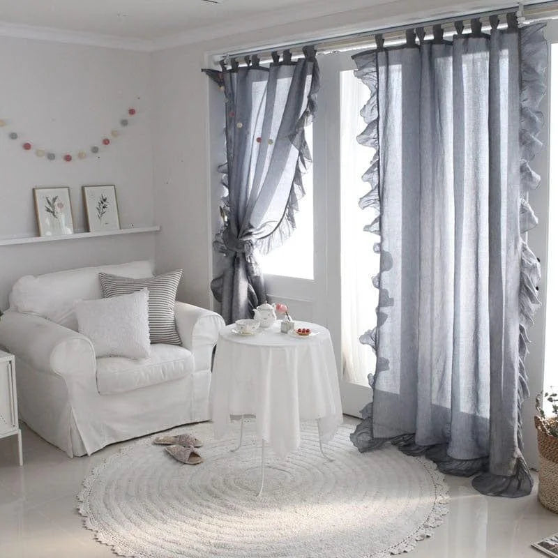 Rideaux élégants dans un salon moderne avec une ambiance lumineuse et apaisante. Le décor comprend un fauteuil confortable, une petite table ronde blanche et un tapis assorti, parfait pour créer un espace détente. Le coloris gris des rideaux ajoute une touche de sophistication et complète harmonieusement ce cadre accueillant.