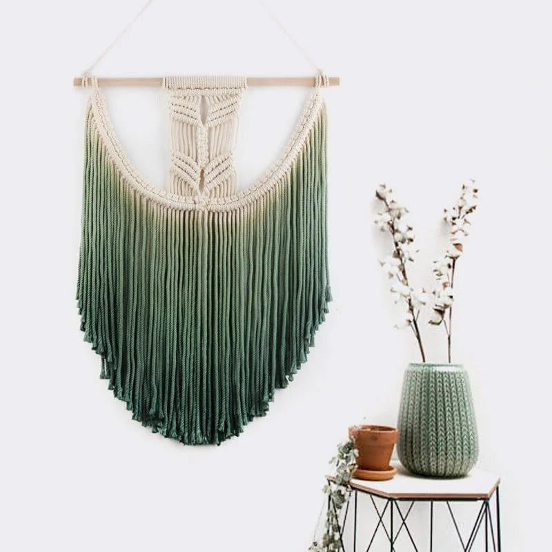 Décoration murale bohème avec dégradé de vert suspendue sur une baguette en bois, ajoutant une touche naturelle à l'intérieur. Cette tapisserie artistique complète parfaitement une ambiance zen, avec des éléments végétaux et une table d'appoint au design moderne. Idéal pour un salon ou une chambre.