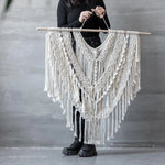 Décoration murale en macramé de style bohème suspendue à une tige en bois. Élément décoratif idéal pour apporter une touche artistique et élégante à votre intérieur. Conçu avec des motifs complexes et des franges, ce macramé s’adapte parfaitement à un salon moderne ou une chambre cosy.