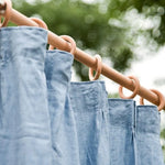 Rideaux bleu clair accrochés à une tringle en bois avec des anneaux, suspendus en extérieur. Idéal pour les espaces de vie naturels, ajoutant une élégance simple et une touche de décoration naturelle à votre intérieur.