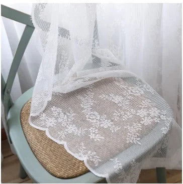 Voilage en dentelle florale blanche délicatement posé sur une chaise en rotin, apportant une touche romantique et vintage à la décoration intérieure.