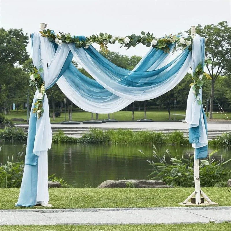 Arche de mariage élégante décorée de drapés bleu et blanc, ornée de feuillage, idéal pour une cérémonie en plein air près d'un lac. Créez une ambiance romantique et naturelle avec ce décor de mariage en extérieur.
