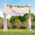Arche de mariage romantique en plein air avec drapés roses et décorations florales vertes, installée sur une pelouse verte devant des arbres, idéale pour une cérémonie nuptiale élégante et naturelle. Accessoire parfait pour un mariage champêtre ou bohème en extérieur.
