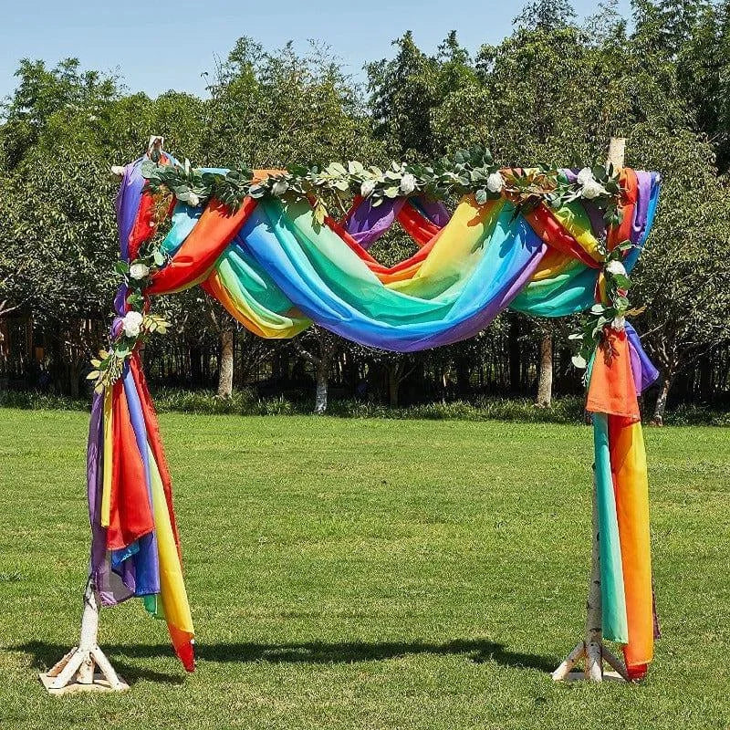Arche de cérémonie colorée en plein air, idéale pour les mariages ou événements festifs. Ornée de tissus aux couleurs de l'arc-en-ciel et de feuillages, elle crée un cadre enchanteur pour vos réceptions en extérieur. Parfaite pour ajouter une touche de gaieté et d'élégance à votre décor.