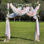 Arche de mariage élégante avec drapés pastel, ornée de feuillage vert et fleurs blanches. Parfaite pour une cérémonie en plein air, elle ajoute une touche romantique à votre événement. Idéale pour les mariages champêtres, offrant une ambiance magique et sophistiquée dans un cadre naturel.