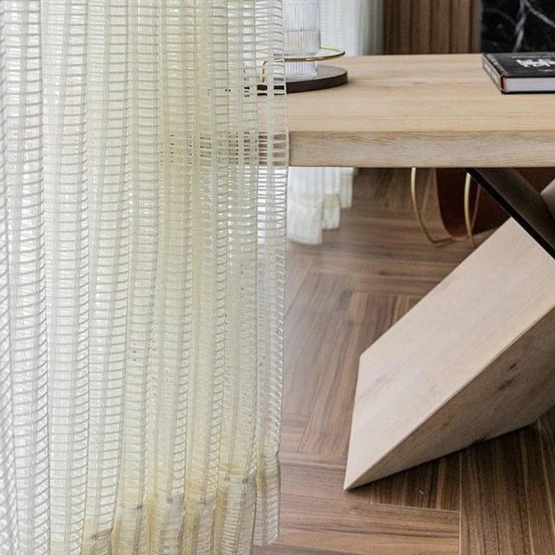 Rideau élégant blanc translucide avec motifs géométriques suspendu devant une table moderne en bois clair. Parfait pour apporter une ambiance lumineuse et contemporaine à votre intérieur. Idéal pour une salle à manger ou un salon, ce rideau ajoute une touche de style et de sophistication.