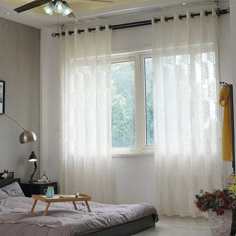 Chambre moderne avec rideaux blancs transparents offrant une ambiance lumineuse, dotée d'un lit confortable et d'une table de nuit, parfaite pour créer un espace cosy et apaisant.