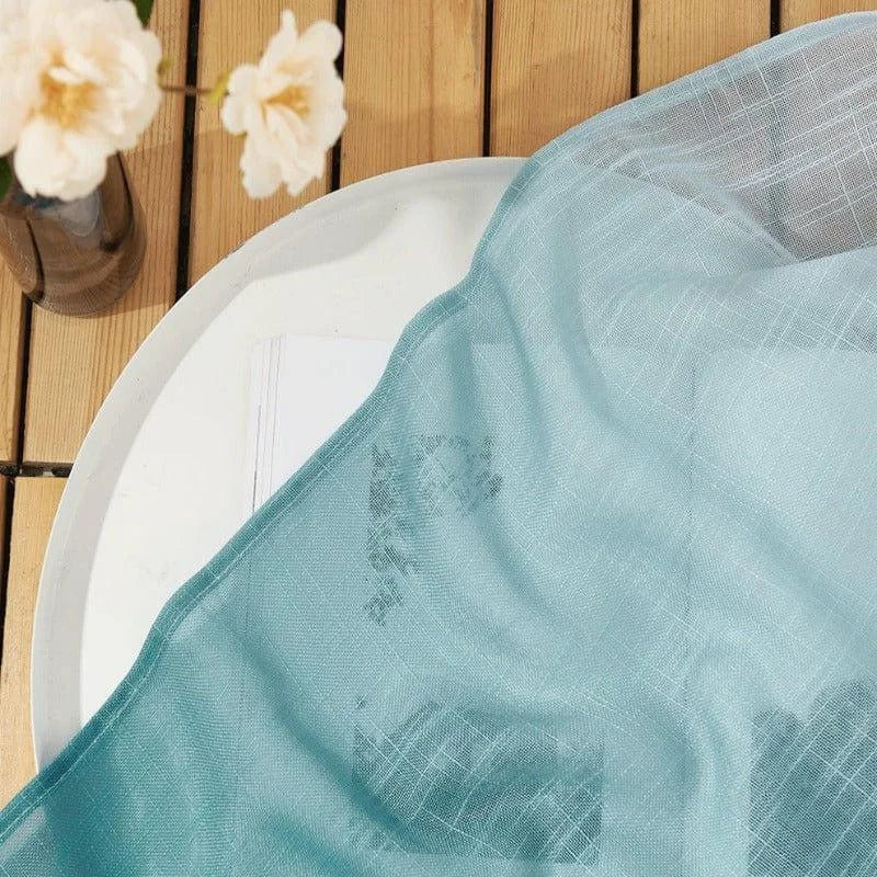 Voile léger bleu drapé sur une table en bois, avec des fleurs blanches délicates dans un vase, parfait pour un décor élégant et minimaliste. Accessoire idéal pour sublimer votre intérieur avec une touche de fraîcheur et de sophistication naturelle.
