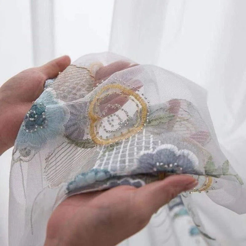 Voile décoratif brodé avec motifs floraux délicats, idéal pour embellir les fenêtres ou créer des rideaux élégants. Ce textile raffiné, orné de détails perlés, ajoute une touche d'élégance et de charme à votre intérieur, parfait pour les salons ou les chambres à coucher. Transformez votre espace avec ce voilage chic et artistique.