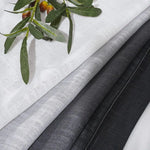 Étoffes élégantes en nuances de gris et blanc, présentées avec un accent naturel de feuilles décoratives, idéales pour la décoration intérieure et la confection de rideaux ou d'ameublement.