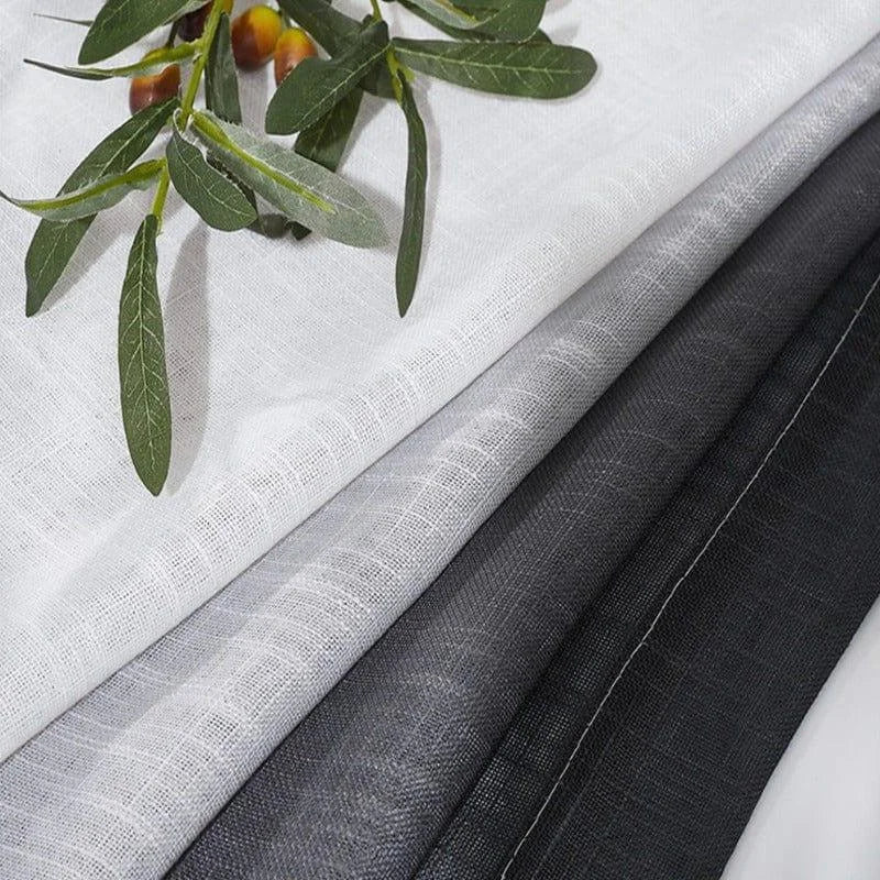 Étoffes élégantes en nuances de gris et blanc, présentées avec un accent naturel de feuilles décoratives, idéales pour la décoration intérieure et la confection de rideaux ou d'ameublement.