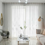 Salon moderne et élégant avec rideaux translucides blancs ornés de motifs floraux discrets, diffusant une lumière douce. Mobilier contemporain comprenant un canapé confortable, une chaise moderne, et une table basse avec des accessoires décoratifs minimalistes. Ambiance épurée et lumineuse, parfaite pour un espace de détente raffiné.
